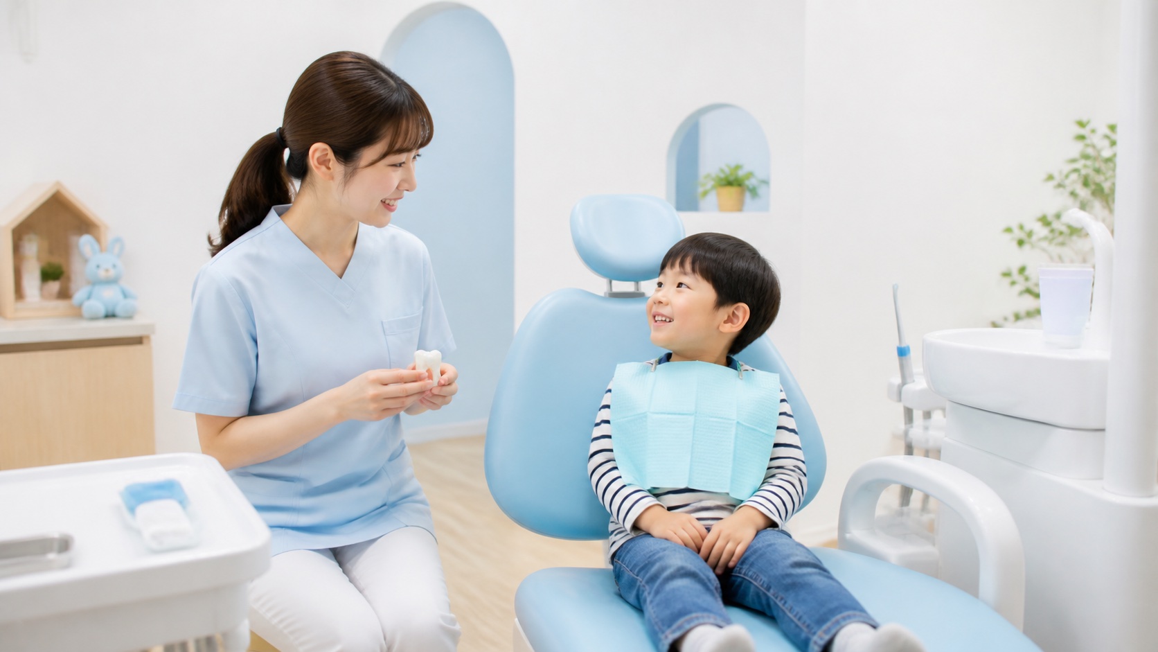 水色の子ども用診療チェアに座った子どもと、笑顔で話す女性スタッフ